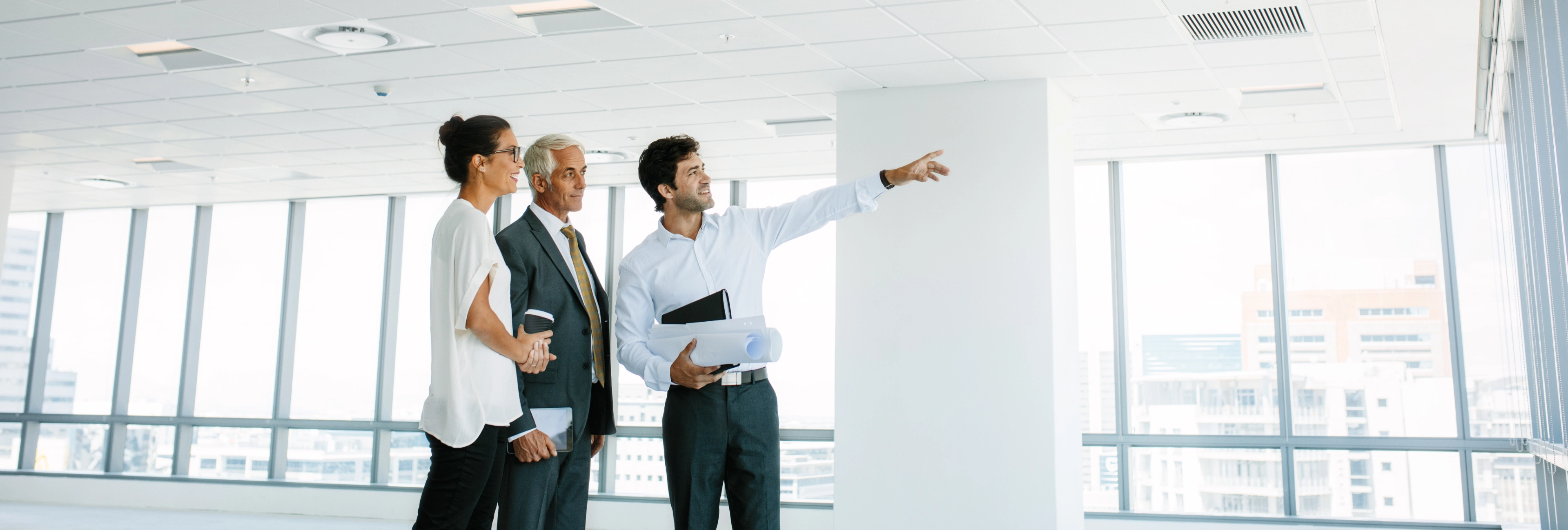 Business professionals and architect reviewing blueprints and pointing at construction plans in bright modern office space