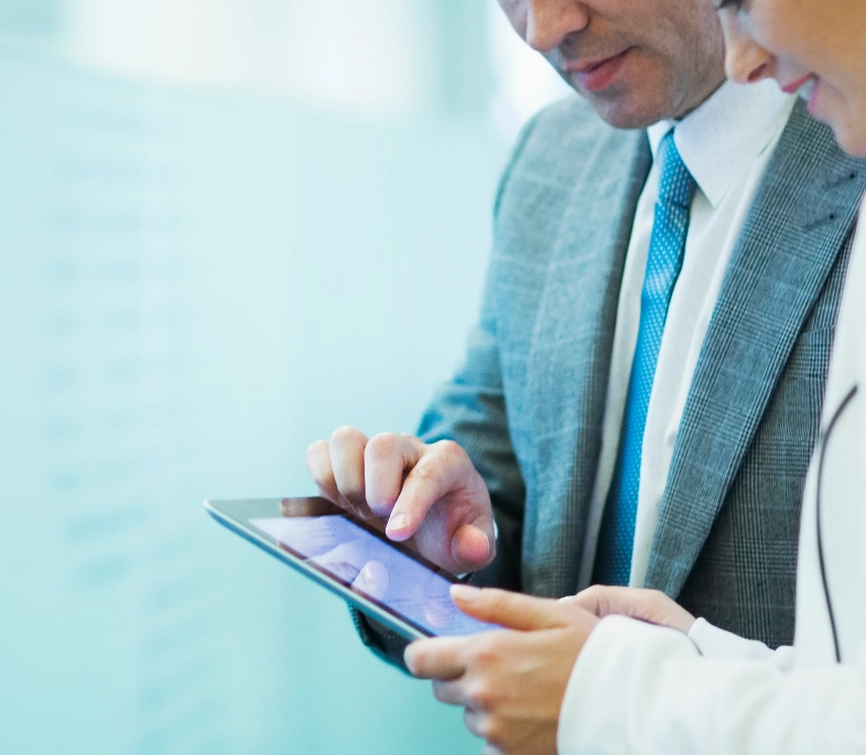 Business professional in gray suit and blue tie using digital tablet in modern office with glass wall background