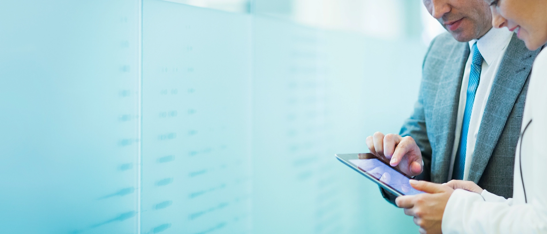 Business professional in gray suit and blue tie using digital tablet in modern office with glass wall background