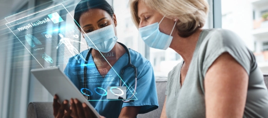 Healthcare worker in blue scrubs with stethoscope discussing digital medical records on tablet with masked patient in clinic