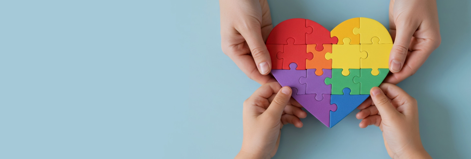 Hands assembling colorful rainbow heart puzzle representing nonprofit teamwork collaboration and purpose-driven unity