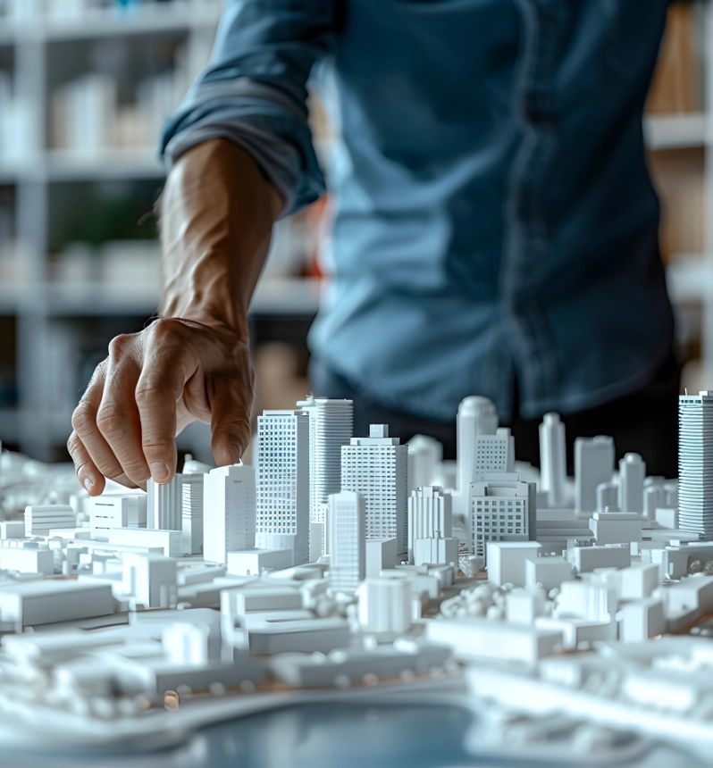 Architect's hand pointing at white miniature city model with skyscrapers representing urban planning and real estate