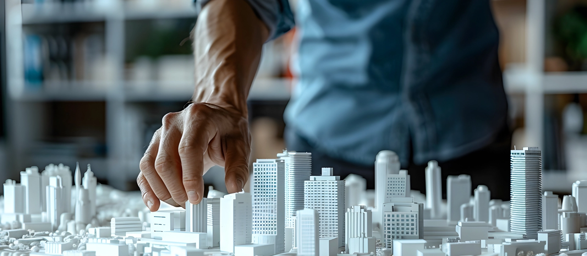 Architect's hand pointing at white miniature city model with skyscrapers representing urban planning and real estate
