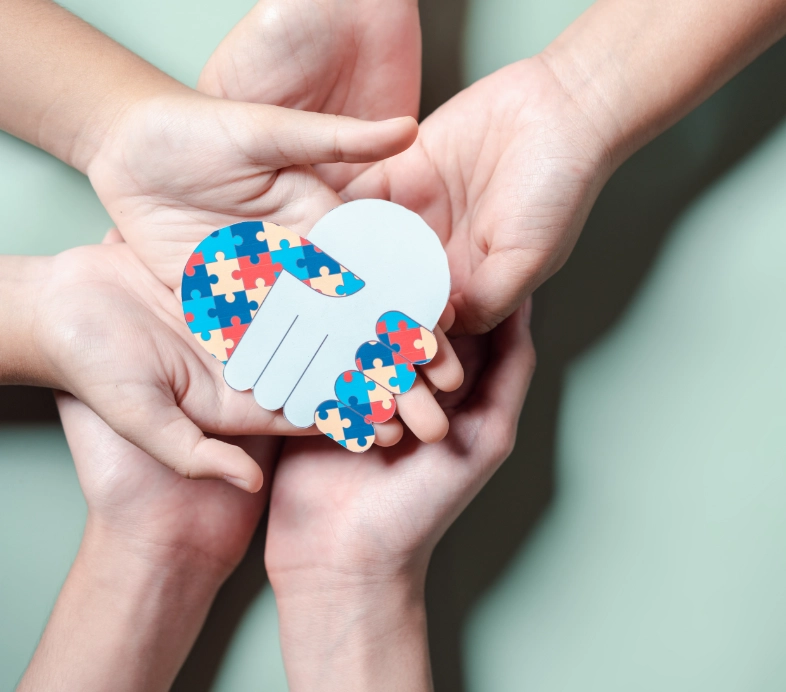 Hands cradling paper brain with colorful puzzle pieces on mint background representing autism awareness and mental health